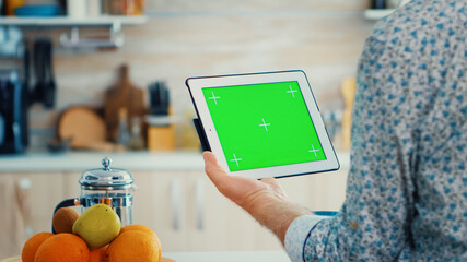 Mature man holding tablet pc with chroma key in kitchen during breakfast. Elderly person with green...