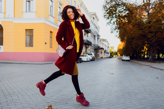 Full length image of  young  black lady in  hat and wool coat jumping  over street background.  Autumn and winter concept.