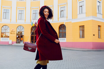 Wonderful young  black lady in  hat and wool coat jumping  over street background.  Autumn and...