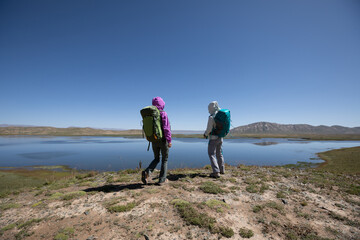 Obraz na płótnie Canvas Two bckpackers enjoy the view on high altitude lakeside