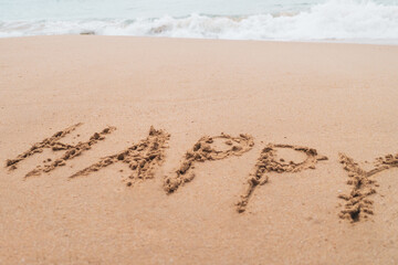 Happy word hand drawn on sand summer beach.