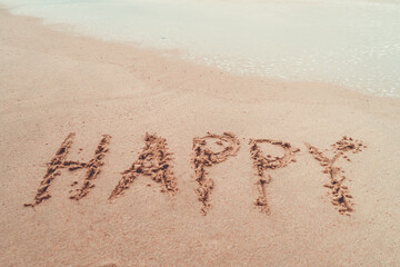 Happy word hand drawn on sand summer beach.