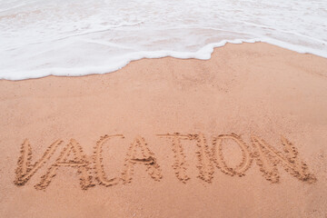 Vacation word hand drawn on sand summer beach.