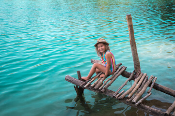 Alone little girl sitting on pier on beautiful blue lake. clean blue water. Wild nature and...