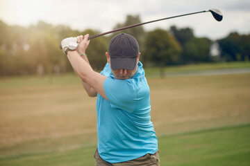 Man playing golf swinging at the ball as he plays his shot using a driver viewed from behind looking down the fairway in a healthy active lifestyle concept