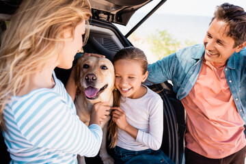 Selective focus of woman petting golden retriever near daughter and husband while traveling in car