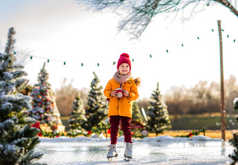 Young boy holding Santa's cup of cacao with marshmallows standing on a fake ice rink.
