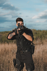 Young soldier in black uniform aiming an assault rifle.