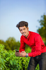 young indian agronomist analyzing field with smartphone