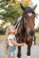 Friendship of a child with a horse. A little girl is affectionately stroking her horse. Walking girls with a horse in the park in autumn.