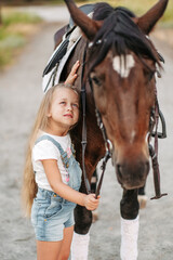 Friendship of a child with a horse. A little girl is affectionately stroking her horse. Walking girls with a horse in the park in autumn.