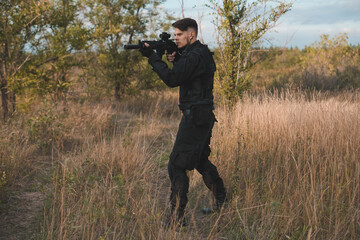 Young soldier in black uniform aiming an assault rifle.