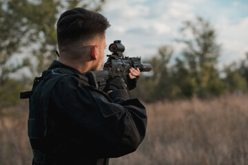 Young soldier in black uniform aiming an assault rifle.