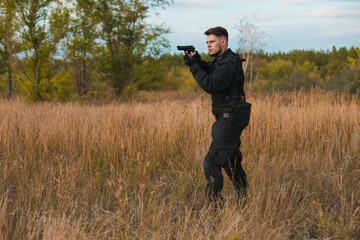 Young soldier in black uniform aiming a pistol. Copy space.