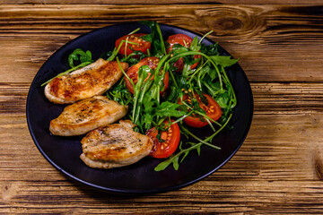 Roasted chicken breasts and salad with arugula and cherry tomatoes in a black plate