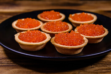 Tartlets with red caviar on a black plate. Festive food