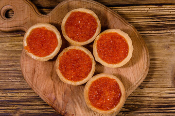 Tartlets with red caviar on a wooden cutting board. Festive food. Top view