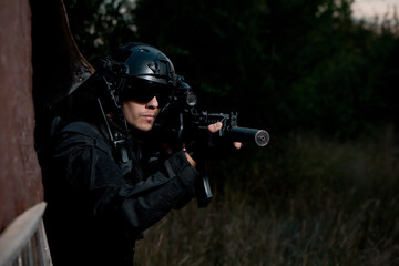 Special force soldier in black uniform helmet and glasses aiming an assault rifle. Copy space