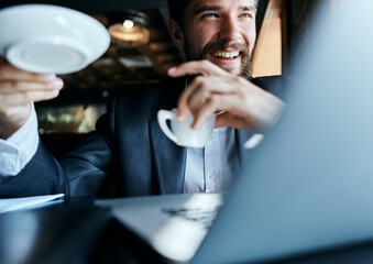 Business man sitting in a cafe with a cup of coffee in his hands in front of a laptop technology communication