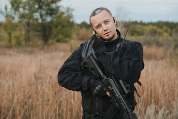 Special forces soldier in black uniform with an assault rifle speaking on the radio.