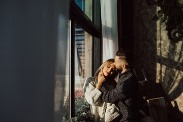 Fototapeta premium Romantic happy young couple relax at home in sunny day. They standing near big window at home.