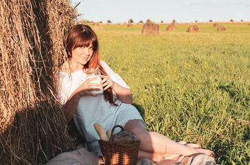 female model plus size having picnic with milk and bread on a field with haystacks, a beautiful young woman with brown hair in white dress, harvest concept