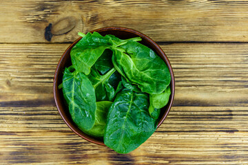 Ceramic bowl with spinach leaves on rustic wooden table. Top view