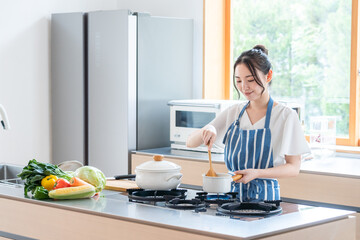 キッチンで料理する若い女性 © polkadot