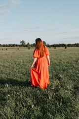 Obraz premium female model plus size in red dress on a field with haystacks, a beautiful young woman with brown hair, harvest concept