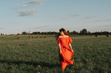 female model plus size in red dress on a field with haystacks, a beautiful young woman with brown hair, harvest concept