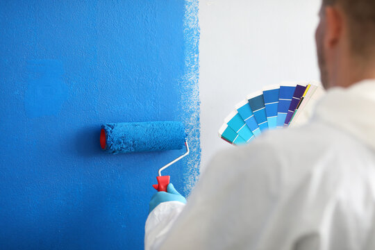 Craftsman holds roller and a color palette and paints white wall blue. Wall painting services and painting concept