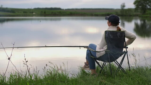 Woman fishing while sitting on a chair by the lake
