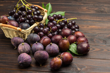 Still life of fruits. Bunch of grapes in wicker basket. Figs and plums on table.