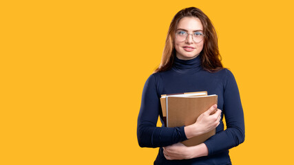 Fototapeta premium Confident woman portrait. Business coaching. Female teacher in eyeglasses standing with books looking at camera isolated on orange copy space background. Personal development. Knowledge skills.