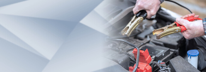 Fototapeta premium Hands of car mechanic using car battery jumper cable; panoramic banner