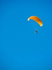 Paraglider flying in blue sky.