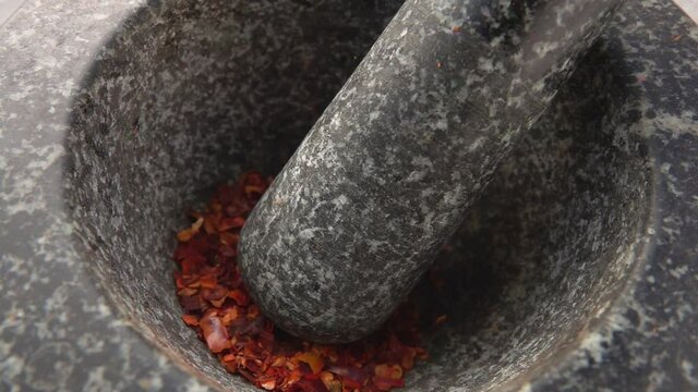 Pieces of red hot chilli pepper are falling into the stone mortar in slow motion