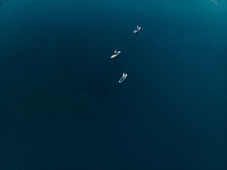 Fototapeta na wymiar Top view of tourists on lake with SUP-boards. Beautiful clear water with people floating on boards engaged in sup-surfing. Seascape with people rowing on boards on background horizon