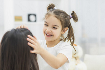 Fototapeta premium Close up photo of happy smiling schoolgirl touching her mother's hair.