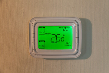 Programmable thermostat to control the air conditioner and heater in a room on the wall. Copy space. Room temperature is set for cooling or heating. Smart home technology increases comfort zone.
