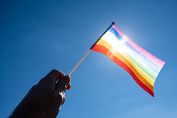 LGBT flag in a man's hand against a blue sky background.