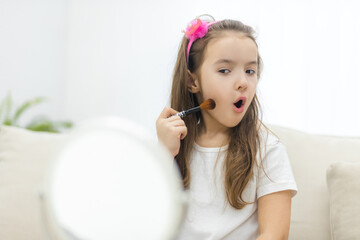 Naklejka premium Photo of little cute girl holding cosmetic brush looking at the mirror on white background.