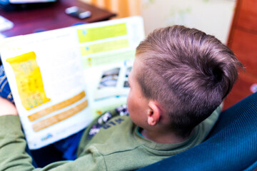 Top view Caucasian nine years old schoolboy reading a book, learning exercise books