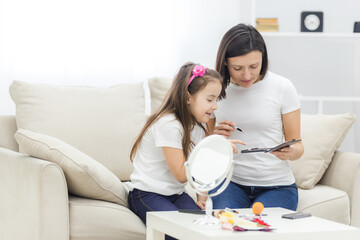 Photo of little daughter helping her young mother with the make up.