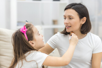 Pretty mother teaching her daughter doing make up at home.