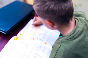 Close up back view of a schoolboy doing homework while sitting at a Desk at home. Reading books and completing lessons.