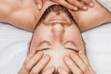 Man receiving relaxing head massage by massage therapist hands, top view.