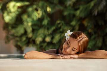 Beauty and body care. Sensual young woman relaxing in outdoor spa swimming pool with flower in the...