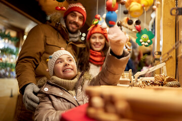 Fototapeta na wymiar family, winter holidays and celebration concept - happy mother, father and little daughter choosing souvenirs at christmas market on town hall square in tallinn, estonia