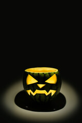 Watermelon carved in the style of Halloween pumpkin. Halloween watermelon glows in the dark. Black background with copy space.